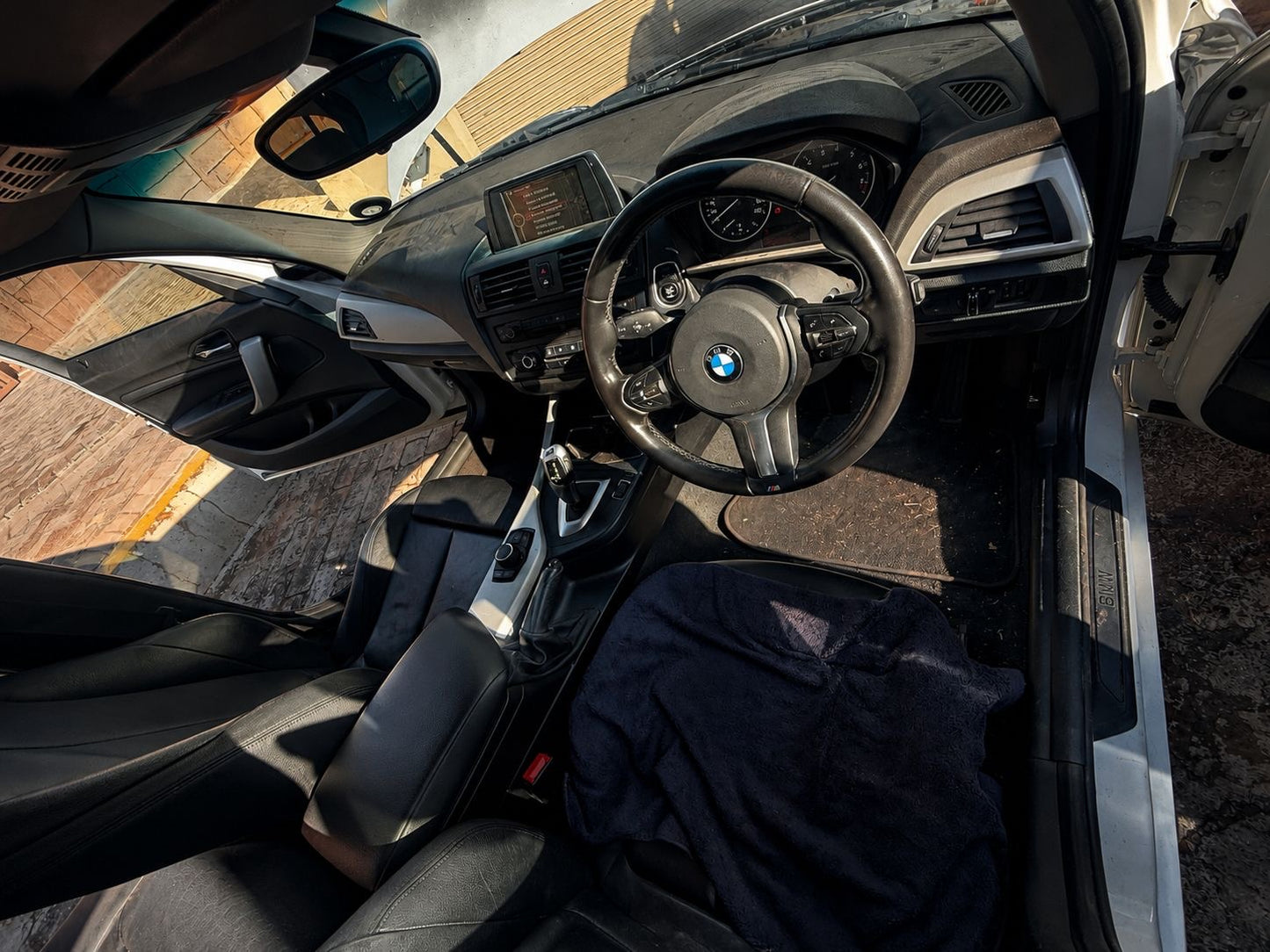 Car interior with steering wheel and dashboard, sun shining through.
