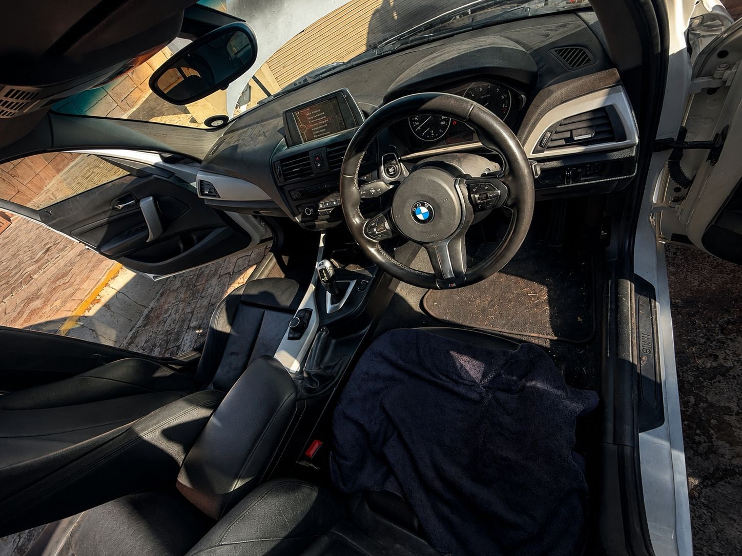 Car interior with steering wheel and dashboard, sun shining through.
