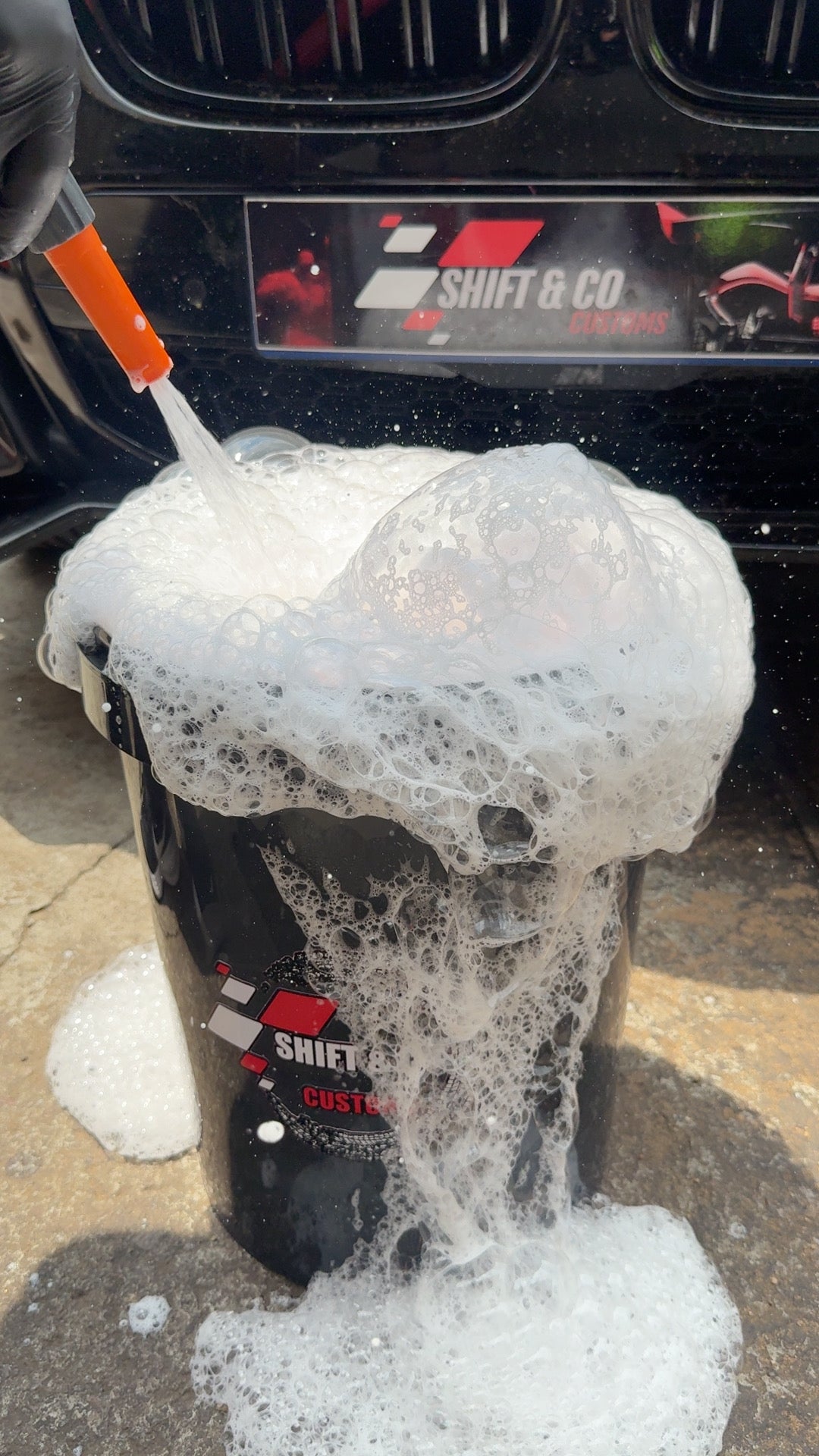 Car wash brush with soap suds on a car surface, with a focus on detailing.