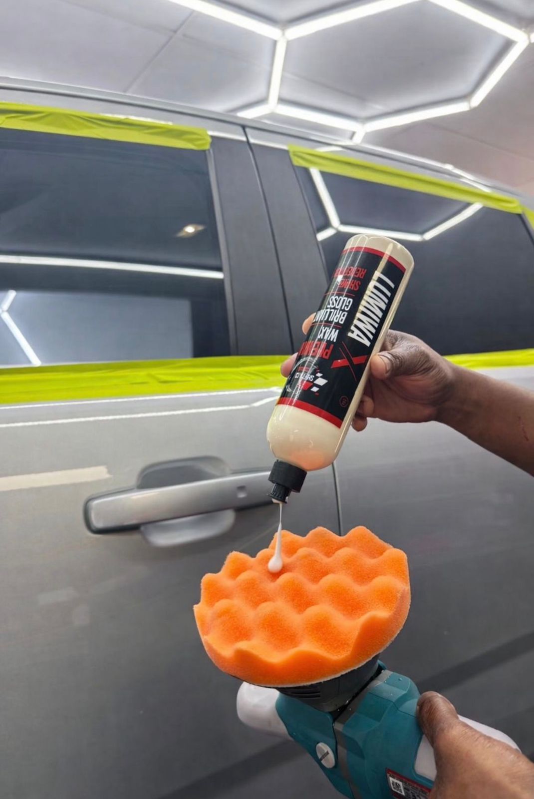 Person using a bottle of car detailing product with an orange foam pad on a car door.